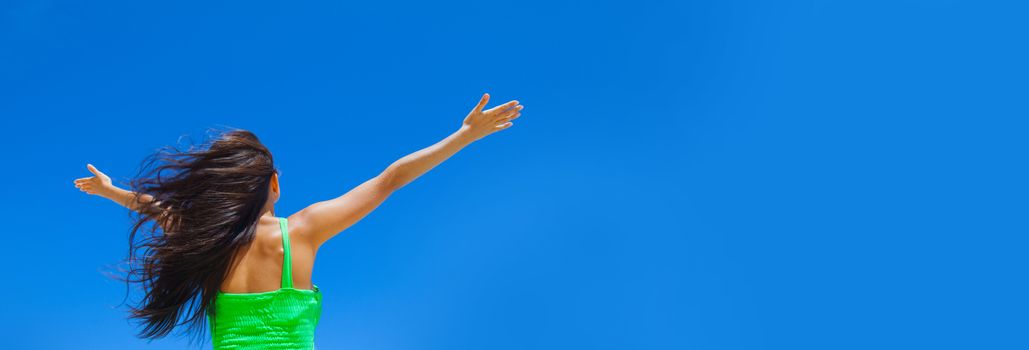 Young woman with raised hands over blue sky background