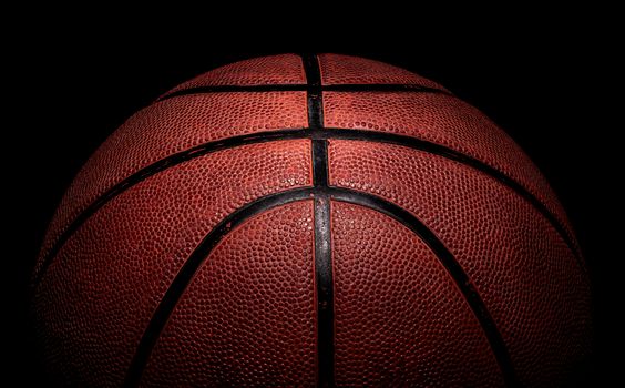 Part of basketball ball illuminated from above. On a black background.