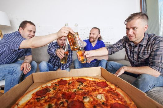 Male friends sitting at home on couch, clink beer, going to eat pizza, celebrating something