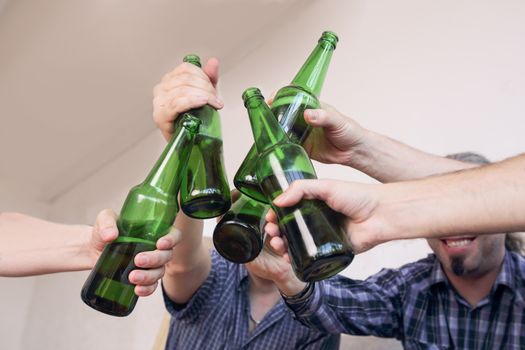 Group of men clinking beer, eating pizza, talking and smiling while resting at home on couch behind TV