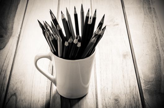 Stack of pencils in a glass on wooden background,tone sepia