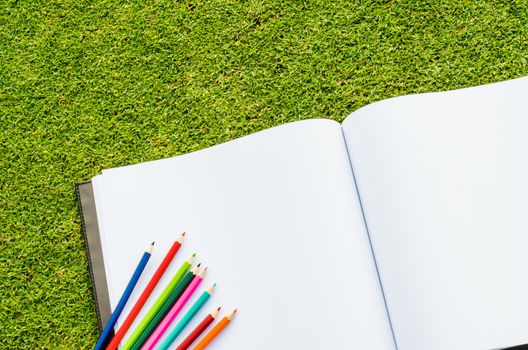 Color pencil and sketchbook on fresh spring green grass