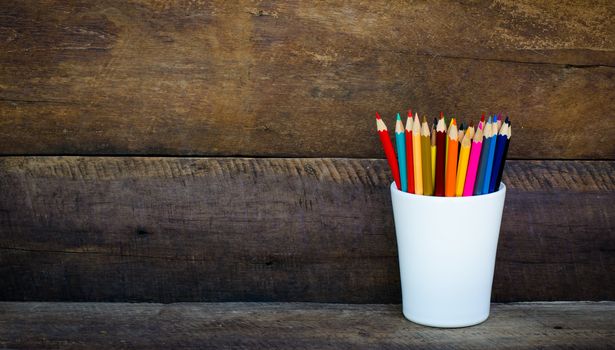 Stack of colored pencils in a glass on wooden background