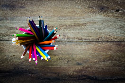 Stack of colored pencils in a glass on wooden background