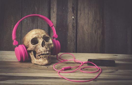 Still life human skull model with pink headphones on wooden background
