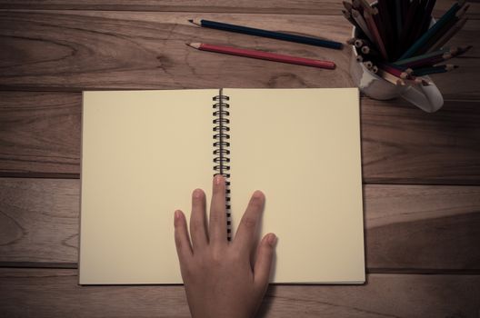 hand and a notebook on a wooden table.