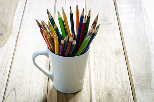 Stack of colored pencils in a glass on wooden background