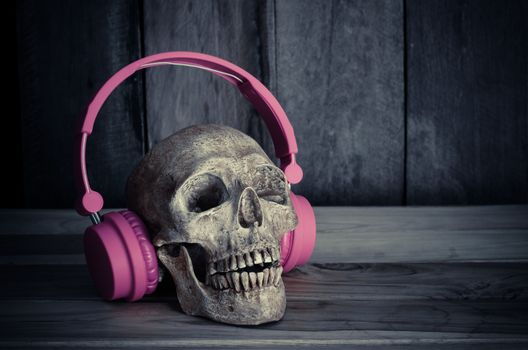 Still life human skull model with pink headphones on wooden background.