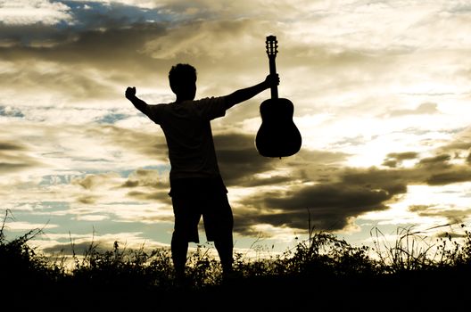 The silhouette of a man holding a guitar nature evening before sunset.