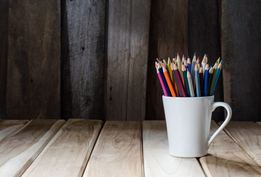Stack of colored pencils in a glass on wooden background
