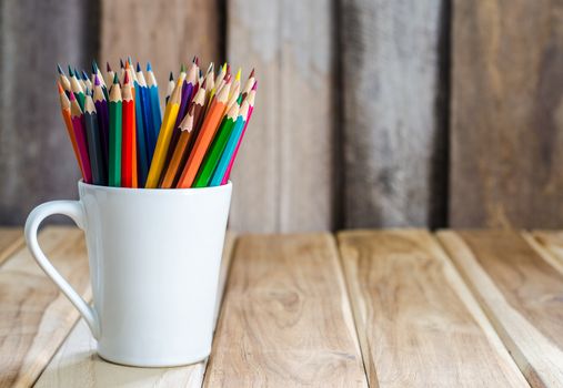Stack of colored pencils in a glass on wooden background