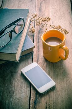 Yellow coffee cup placed on a wooden table with a smart phone, glasses, books, dried flowers - tone vintage