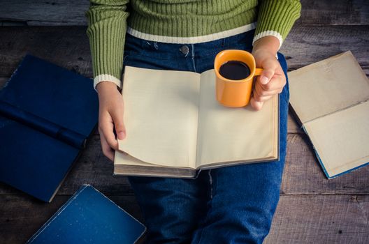 woman is sitting on a wooden floor and reading a book while holding a coffee cup