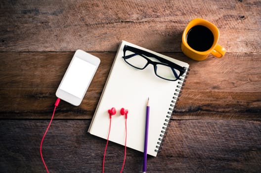 surface of a wooden table with notebook, smartphone, glasses,