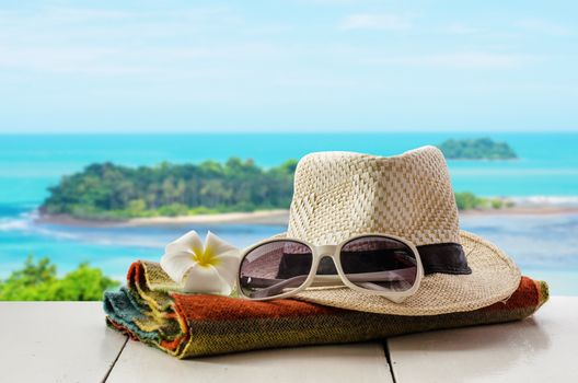 Hats, glasses, scarves, flowers are placed on a wooden floor with the sea as background.