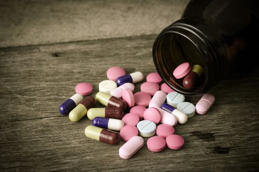 Different types of pills lying on a wooden floor.