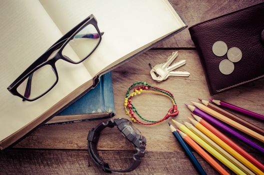 Equipment notebooks, colored pencils, watches, glasses, wallet, coins placed on a wooden floor.