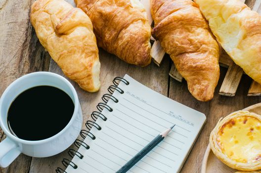 Croissants coffee notebook and pencil on the wooden table - tone vintage