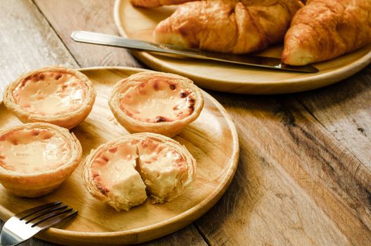 Egg tarts and croissants on a wooden plate on a wooden table.