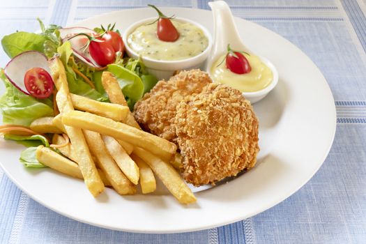 Deep fried fish steak served with french fries and fresh vegetables on white plate