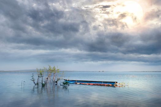 The boat in lake under beautiful rain clouds and sun