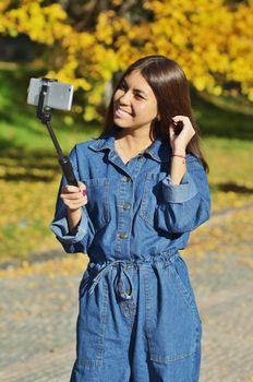 Young beautiful girl in denim suit takes selfie walking in city Park in autumn