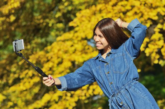 A young beautiful girl in a denim suit takes a selfie walking in the city Park in the autumn, horizontal photo