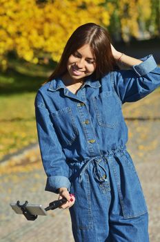 Young beautiful girl in denim suit takes selfie walking in city Park in autumn