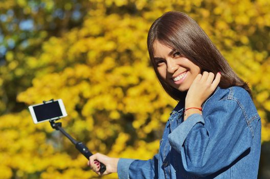 A young beautiful girl student in a denim suit looks at the camera and takes a selfie walking in the city Park in the autumn, horizontal photo