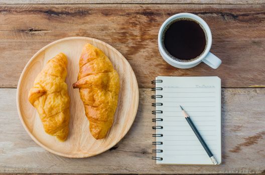 Croissants coffee notebook and pencil on the wooden table - tone vintage