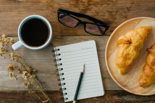 Croissants coffee notebook eyeglasses pencil on the wooden table - tone vintage