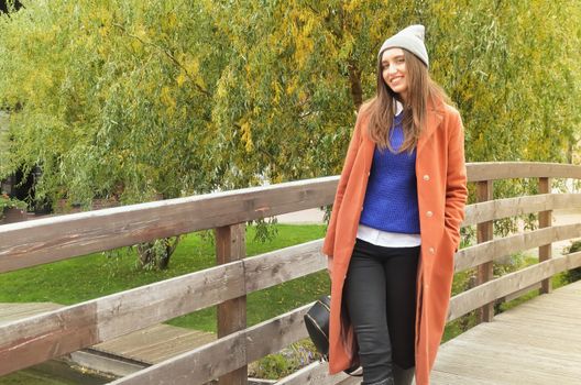 Beautiful girl in a hat and coat standing on the bridge and smiles