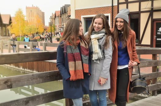 Three girls in a coat on the bridge standing together and laughing