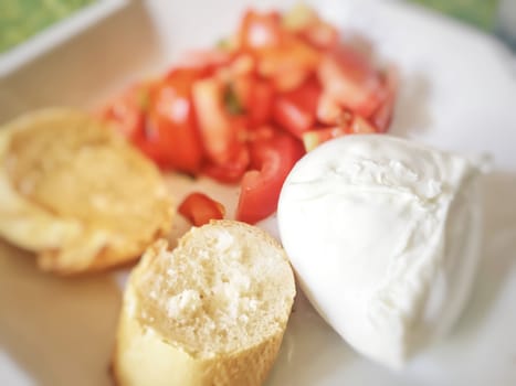 Homemade caprese salad with mozzarella cheese, chopped tomatoes and sliced bread. Italian summer food