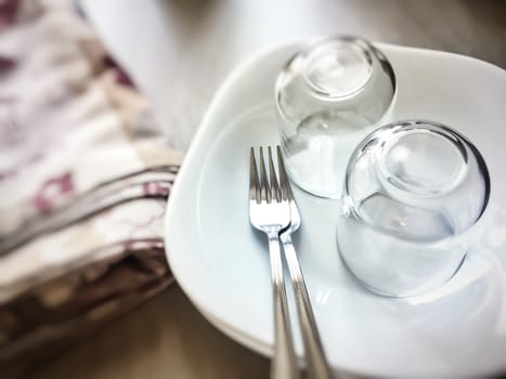 Setting the table for dinner with forks, white plates, glasses and tablecloth