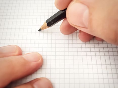 Writing with a pencil on a white sheet of squared paper