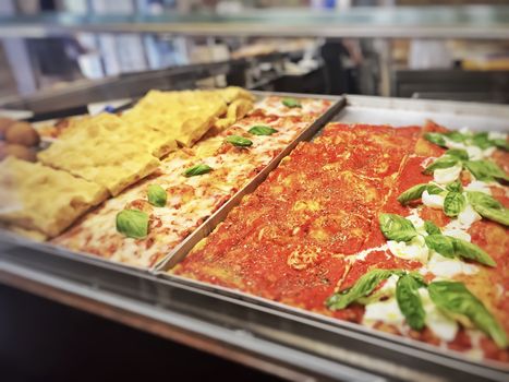 pans with various types of slices of pizza in a pizzeria