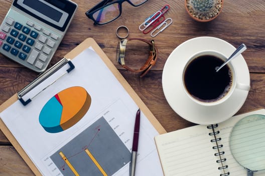 coffee cup, chart, calculator, pen, notebook and accessory for work on wooden table.
