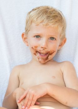 Portrait of fair-haired baby boy with chocolate on his face isolated on white background.