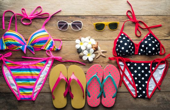 Bikinis, sunglasses, shoes, two sets placed on a wooden floor
