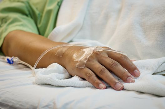 Hand of Male patient lying on a hospital bed receiving saline.