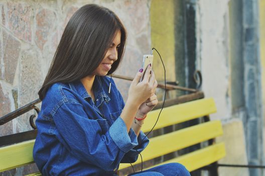 Young beautiful Asian girl sitting on a bench talking on the phone, horizontal photo, campus