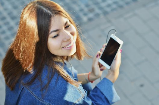 The girl sits on a bench and listens to music with headphones smiling with her eyes closed