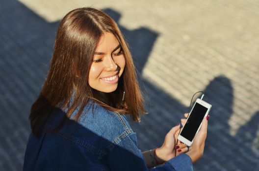 The student sits on a bench and listens to music on the phone with headphones, eyes closed, enjoying the music and the rays of the evening sun