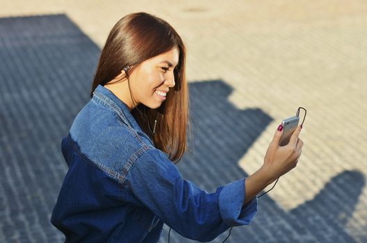 Young cute student talking on the phone by video on the street and smiling holding the phone in front of him