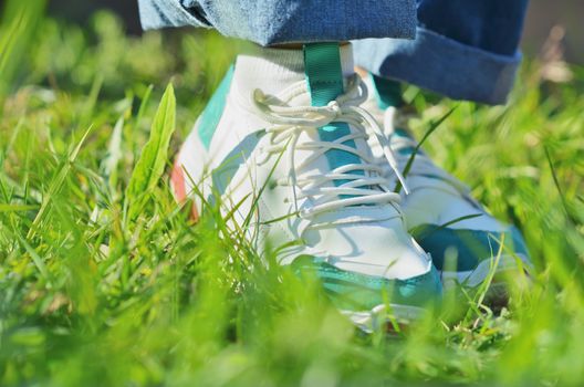 A young girl standing on the green grass in sneakers. Close-up photo