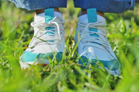 A young girl standing on the green grass in sneakers. Close-up photo