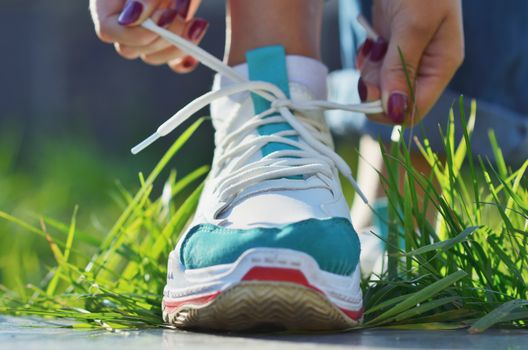 Young girl tying shoelaces on sneaker standing on green grass close-up view horizontal photo, Sunny day