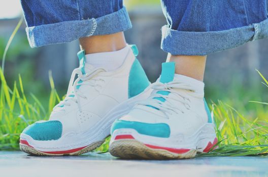 Girl in sneakers standing near the green grass on a Sunny day, side view