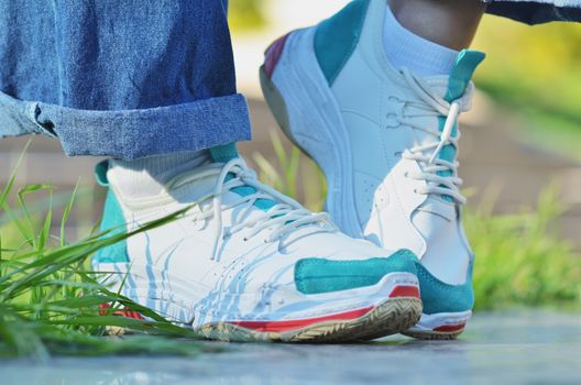 Girl in sneakers standing near the green grass on a Sunny day, side view